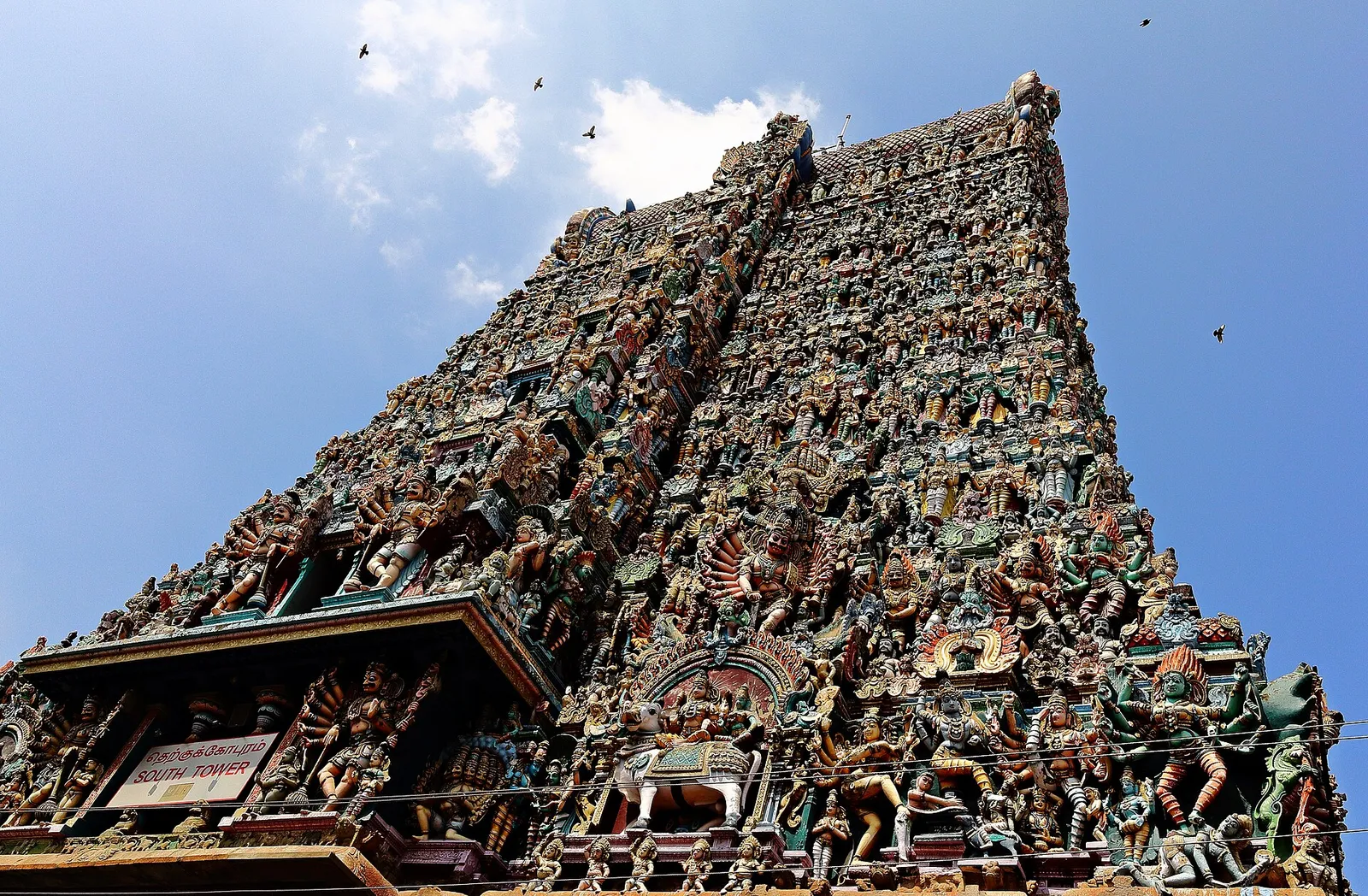 The richly sculpted south gopuram of the Meenakshi Amman Temple in Madurai against a blue sky