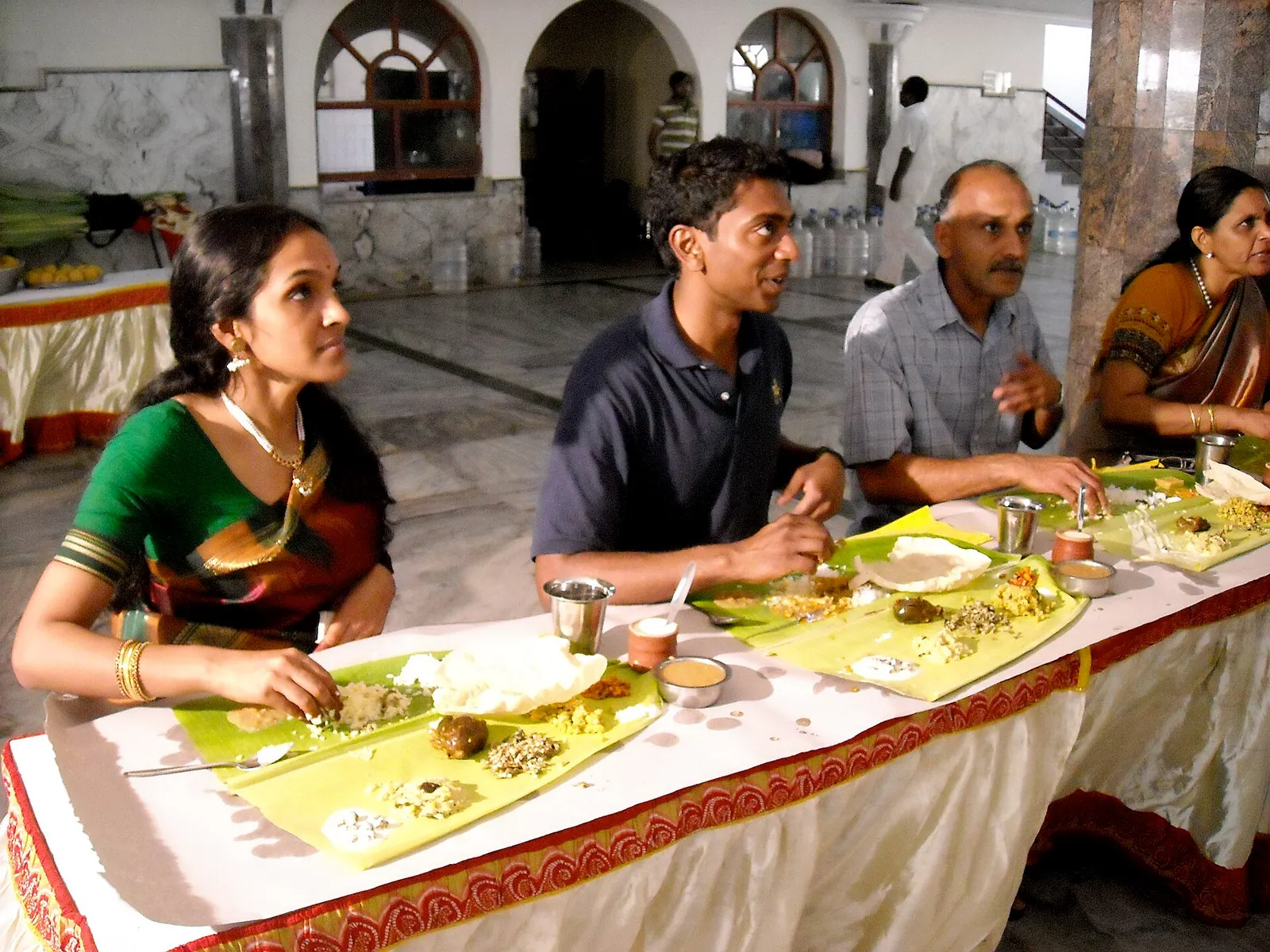 Guests seated at a long table eating a traditional meal served on banana leaves at a wedding