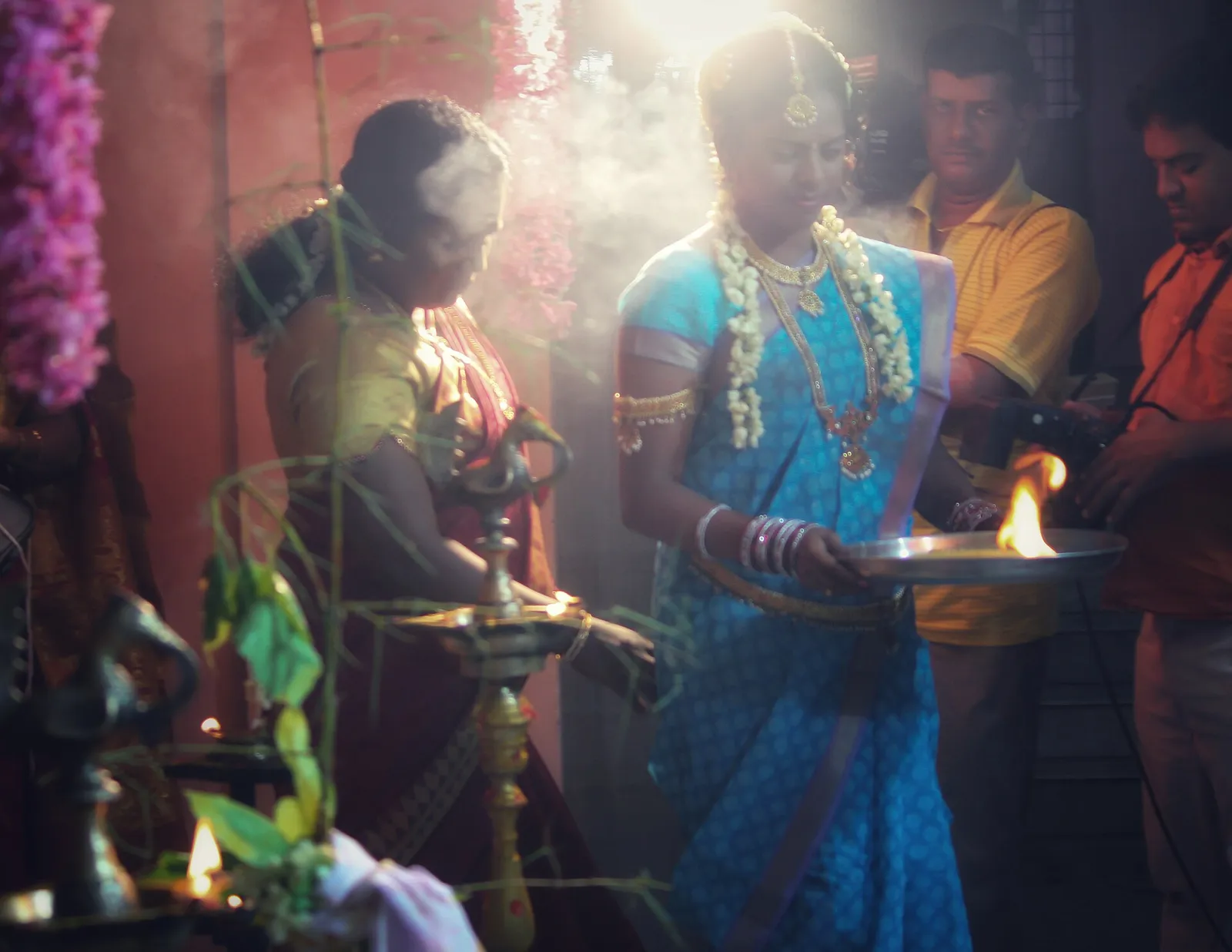 Women in silk sarees perform aarti with a flame on a brass plate in the wedding hall