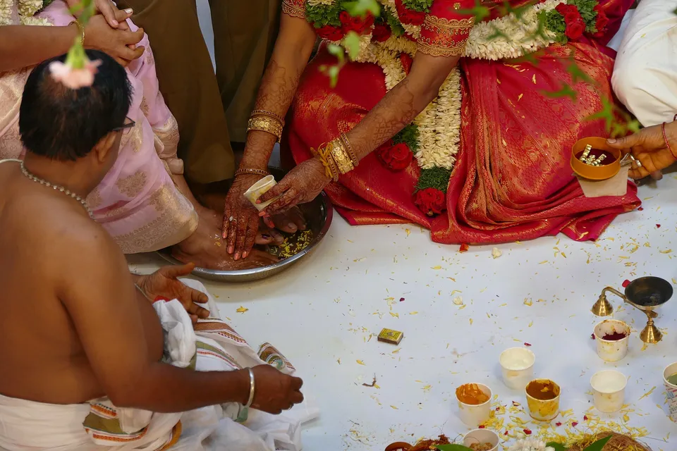 Family members perform the paada pooja for the couple, with brass plates, flowers and lamps around them