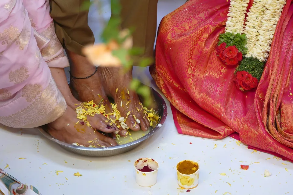 Close-up of feet in a brass plate strewn with flower petals during a wedding ritual