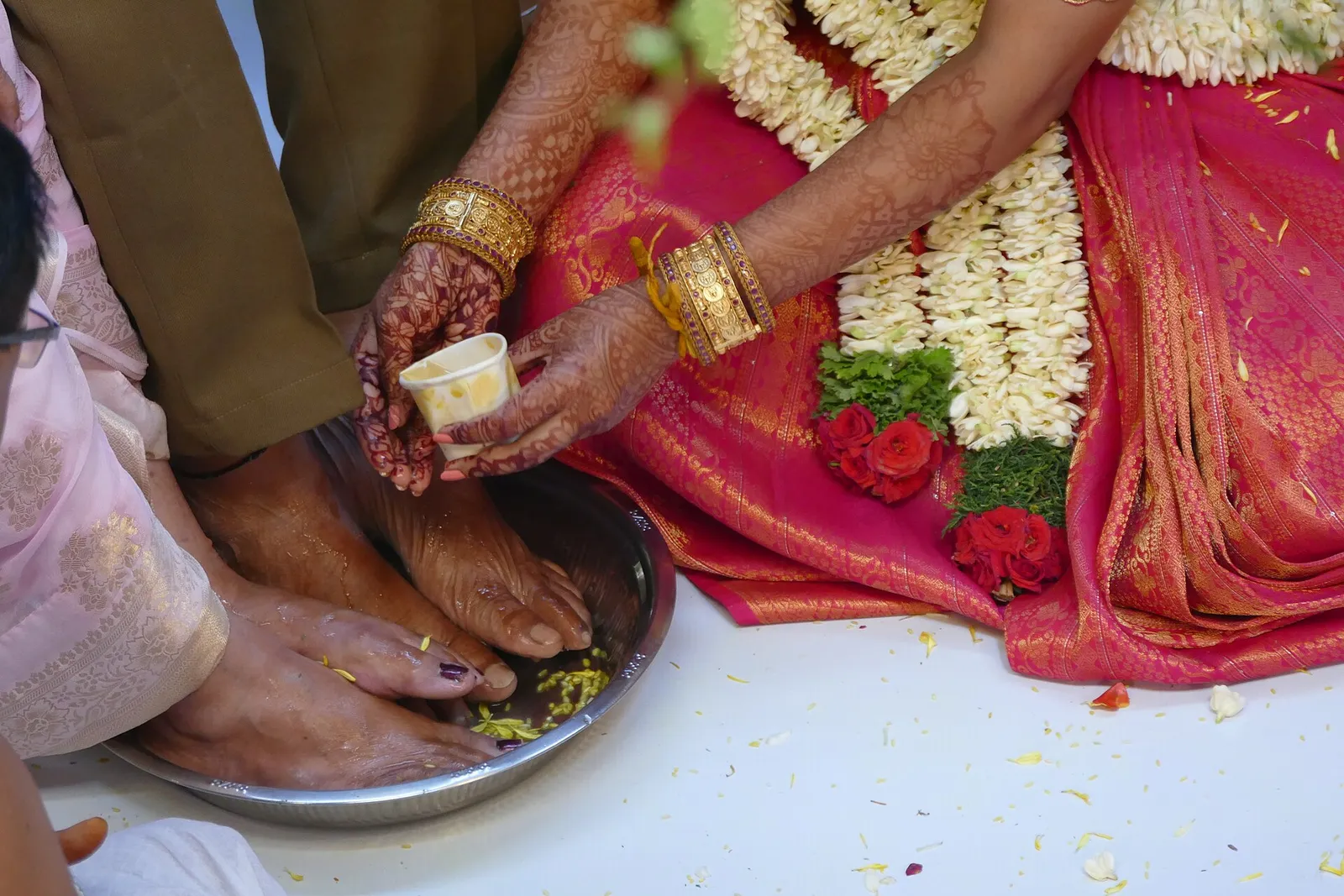 Feet being washed with water and flower petals in a brass plate during a Tamil wedding