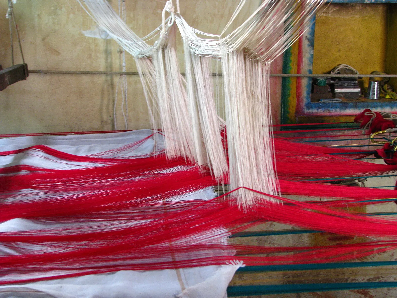 Red and white silk warp threads stretched across a handloom in Kanchipuram
